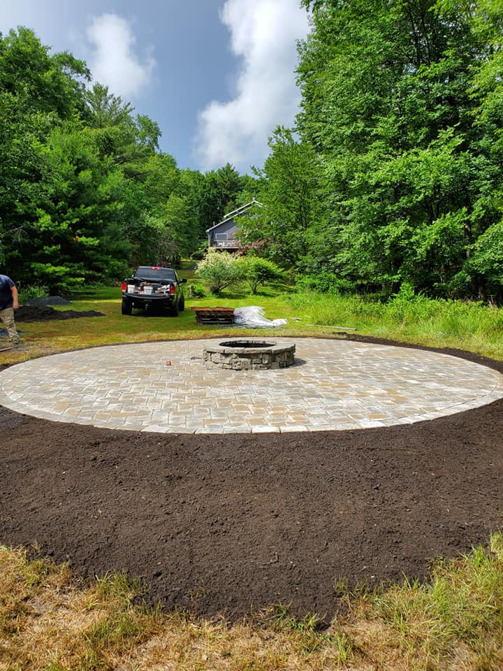 Circular paver patio with stone fire pit by the lake